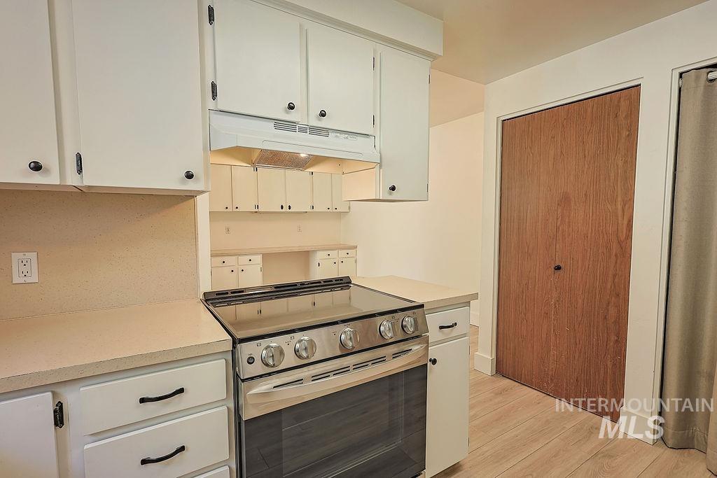 640 Morrison Street Twin Falls, ID 83301 - Photo 11 of 30 Kitchen featuring a stainless steel range with overhead ventilation, white cabinetry with dark hardware, light-colored countertops, and wood-finish flooring