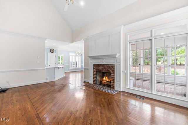 a view of an empty room with wooden floor fire place and windows