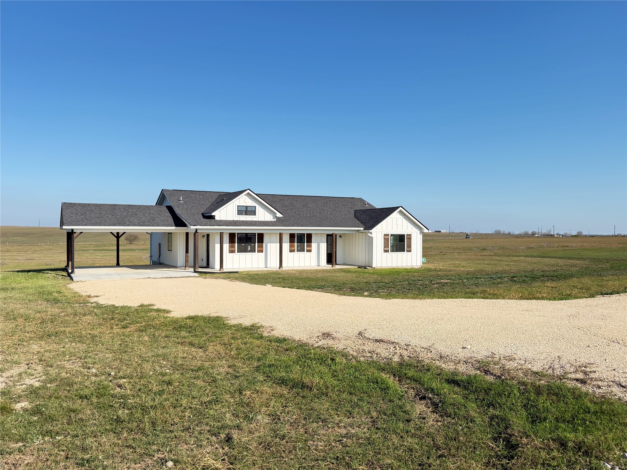 Modern farmhouse featuring a porch, roof with shingles, driveway, a front lawn, and a carport