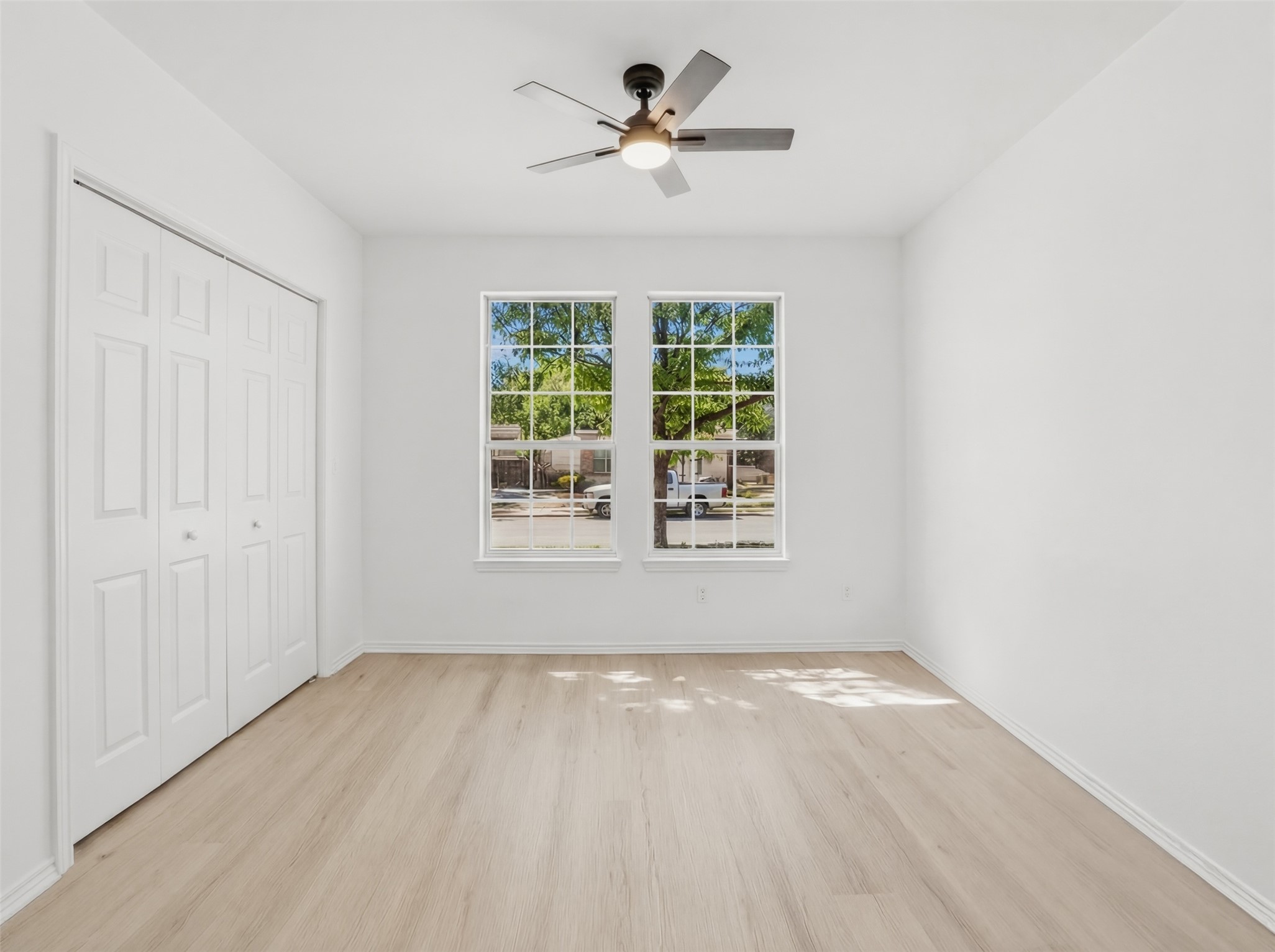 461 Hot Spring Valley Buda, TX 78610 - Photo 18 of 25 This room features light-toned flooring, two windows, a ceiling fan with integrated lighting, and bi-fold closet doors
