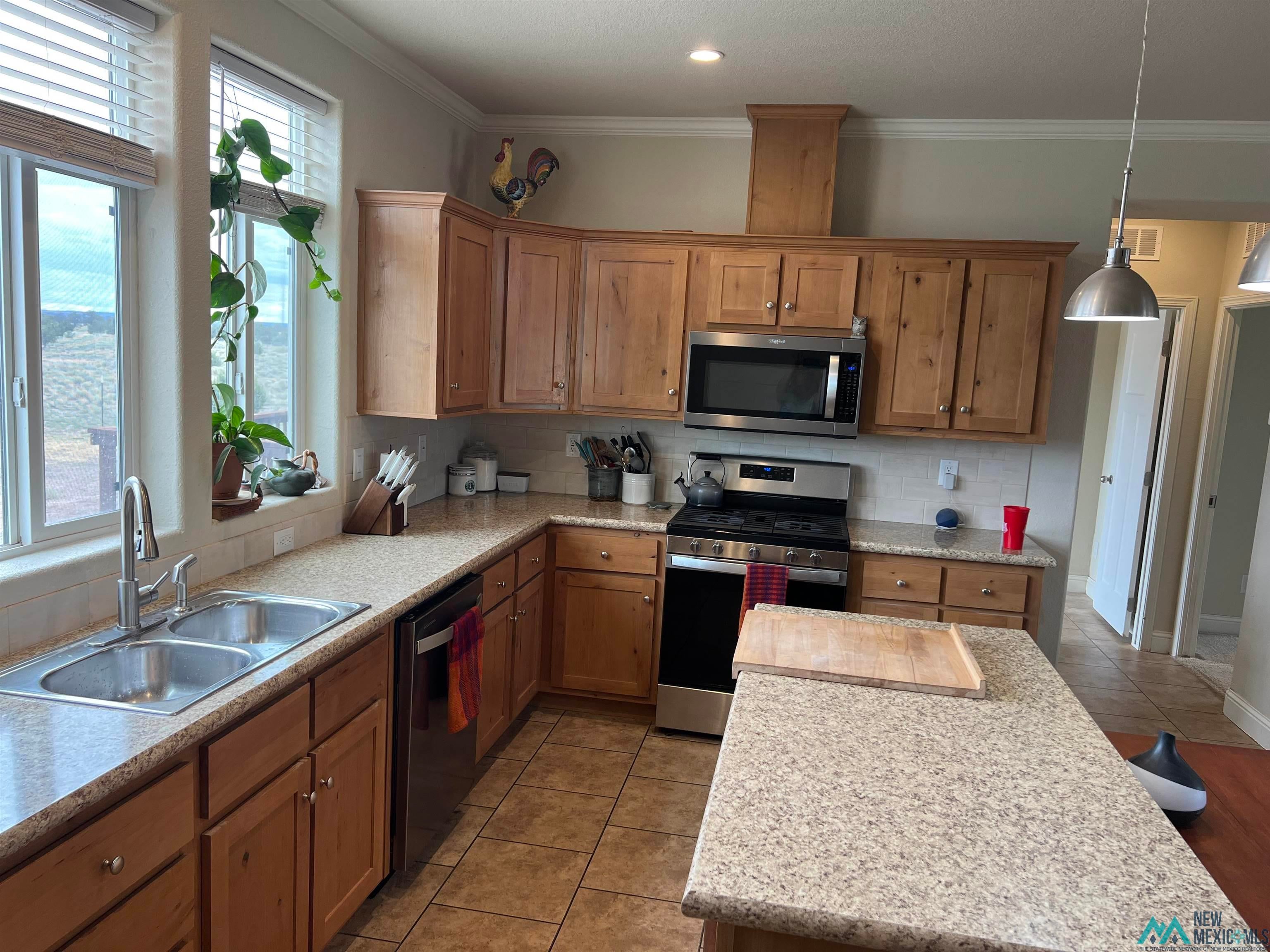 56 Kachina Road Quemado, NM 87829 - Photo 7 of 36 Kitchen with appliances with stainless steel finishes, light tile patterned flooring, tasteful backsplash, hanging light fixtures, and brown cabinets