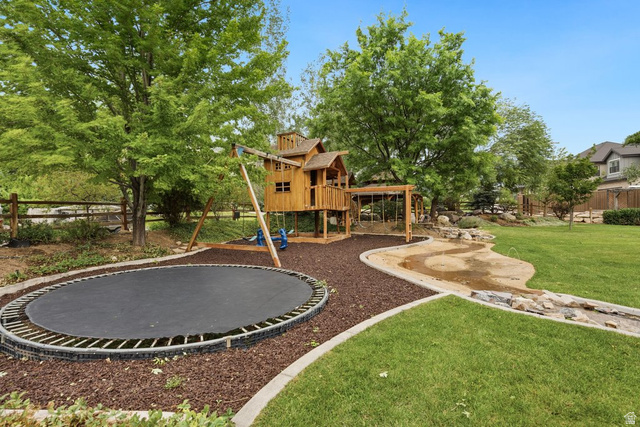 672 Perry Hollow Drive Mapleton, UT 84664 - Photo 96 of 106 Expansive backyard featuring a built-in trampoline, custom wooden play structure with swing set, rock-lined water feature, mature trees, and manicured lawn