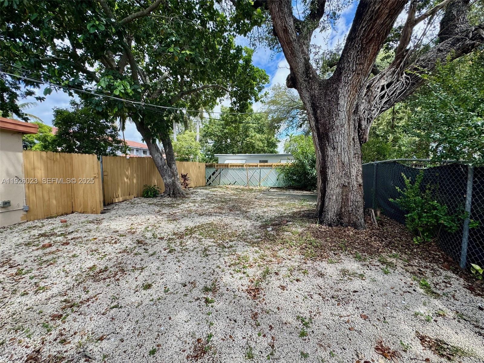 718 Southwest 7th Street, Unit 718 Hallandale Beach, FL 33009 - Photo 11 of 13 a backyard of a house with large trees and a wooden fence
