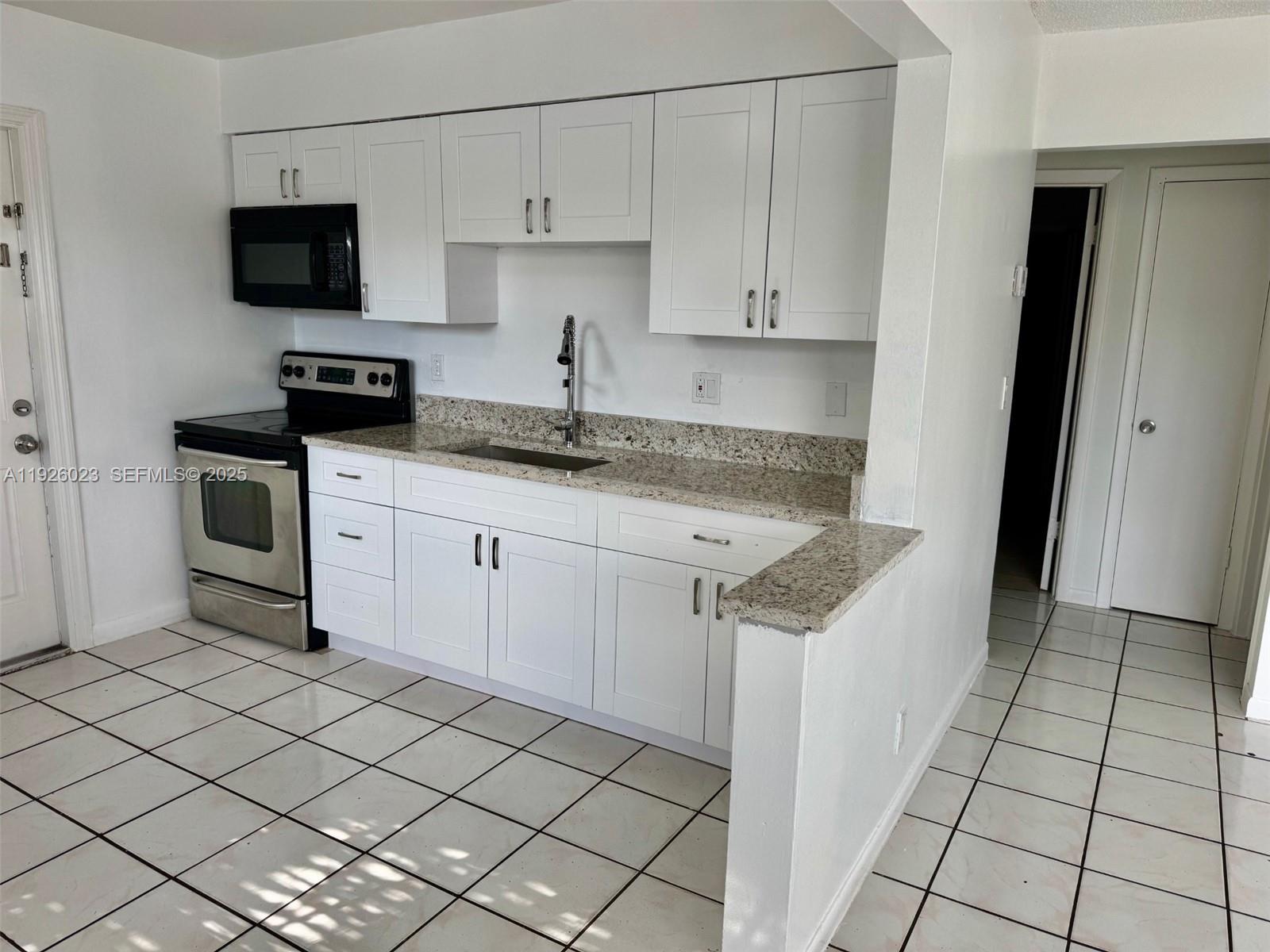 718 Southwest 7th Street, Unit 718 Hallandale Beach, FL 33009 - Photo 5 of 13 a kitchen with granite countertop white cabinets and stainless steel appliances