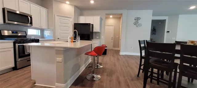 a kitchen with stainless steel appliances granite countertop a stove top oven a refrigerator a sink a dining table and chairs with wooden floor