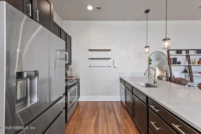 a kitchen with stainless steel appliances a stove a sink a refrigerator white cabinets and wooden floor