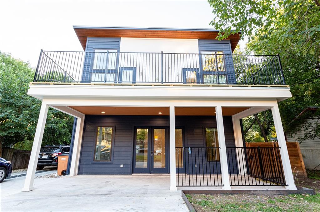 Back of house with a porch, concrete driveway, french doors, and a balcony