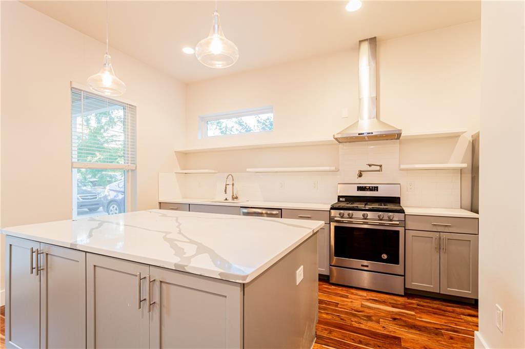 2509 Del Curto Road, Unit B Austin, TX 78704 - Photo 7 of 31 Kitchen featuring gray cabinetry, dark wood finished floors, a sink, wall chimney range hood, and appliances with stainless steel finishes