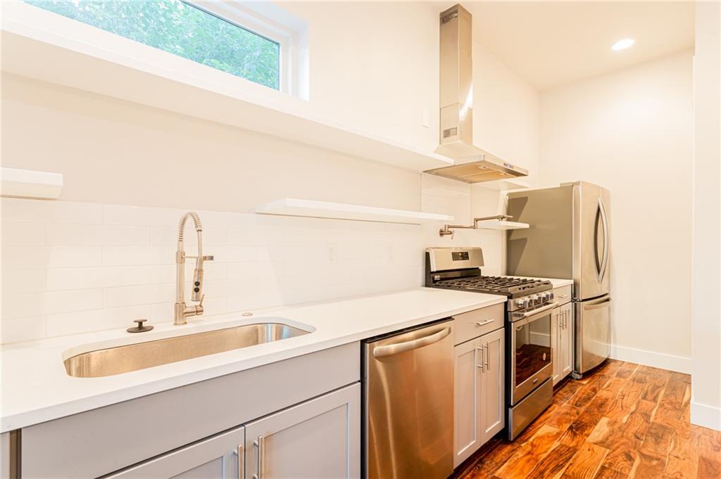 2509 Del Curto Road, Unit B Austin, TX 78704 - Photo 10 of 31 Kitchen with light wood finished floors, a sink, stainless steel appliances, baseboards, and wall chimney range hood
