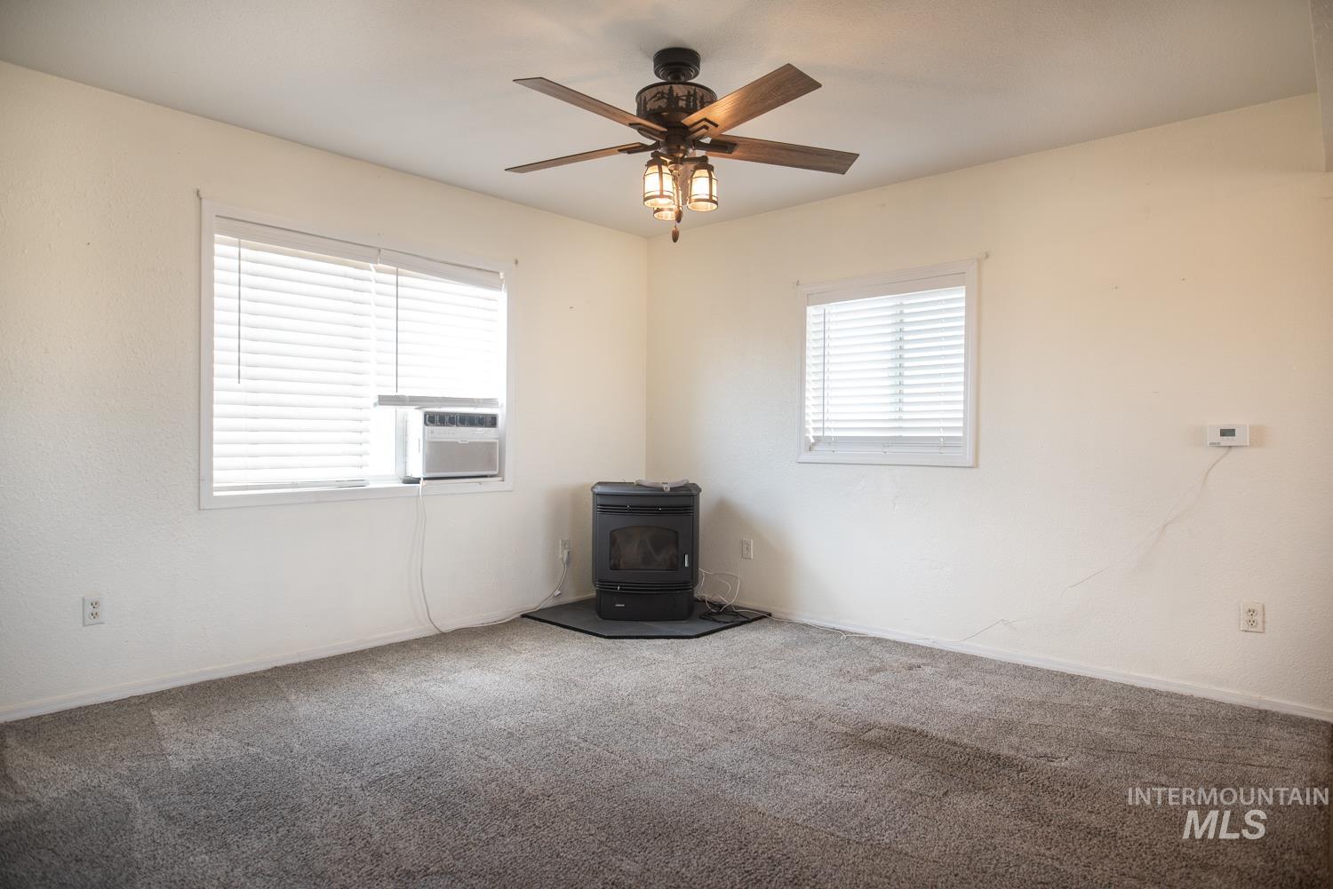 2240 Waite Road Midvale, ID 83645 - Photo 22 of 42 Empty room featuring a wood stove, a ceiling fan, carpet floors, and cooling unit