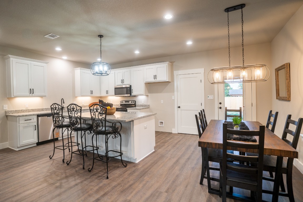 306 String Prairie Way Smithville, TX 78957 - Photo 5 of 25 Kitchen with appliances with stainless steel finishes, a center island, white cabinets, wood finished floors, and light stone countertops