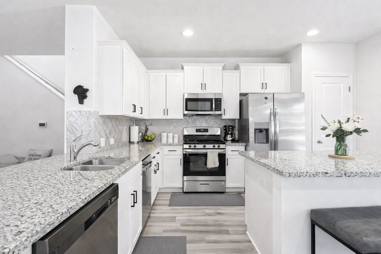 940 Paddock Lane Georgetown, TX 78626 - Photo 14 of 32 Contemporary kitchen featuring white cabinetry, stainless steel appliances, speckled countertops, a herringbone tile backsplash, and wood-finish flooring