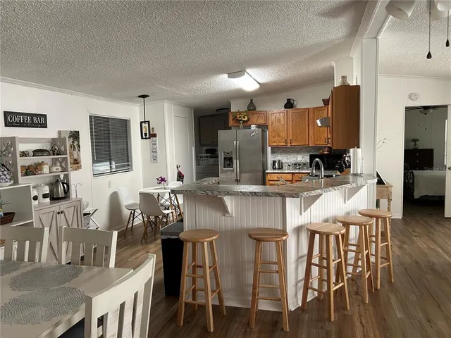 a kitchen with stainless steel appliances kitchen island granite countertop a dining table chairs and a refrigerator