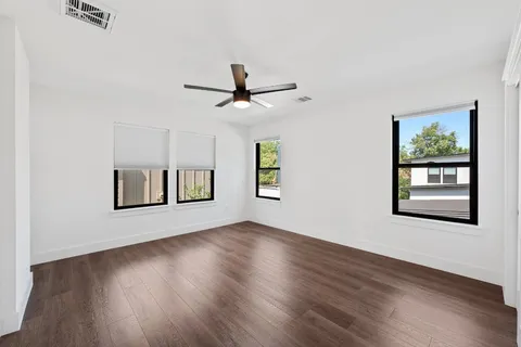a view of an empty room with wooden floor and a ceiling fan