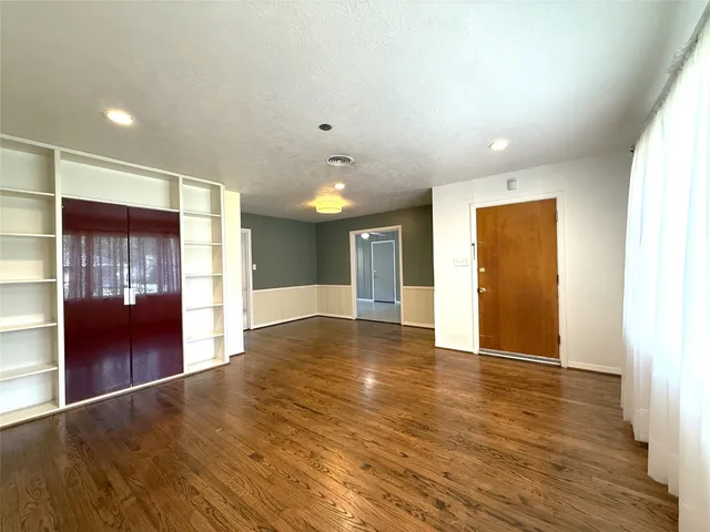 a view of an empty room with wooden floor and a kitchen