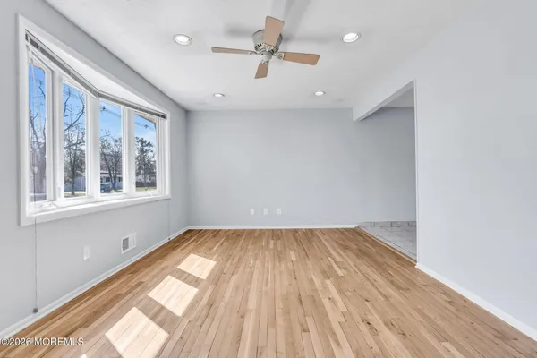 an empty room with wooden floor chandelier fan and windows