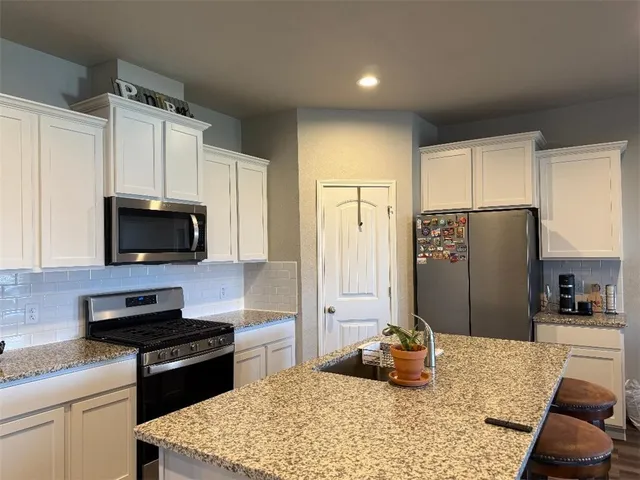 a kitchen with kitchen island granite countertop a refrigerator stove top oven and sink