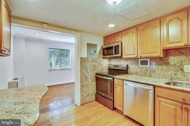 a kitchen with stainless steel appliances granite countertop a refrigerator a stove a sink dishwasher and wooden cabinets with wooden floor