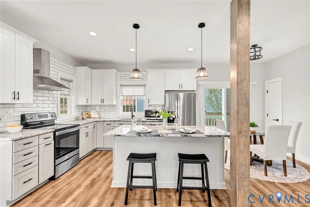 a kitchen with stainless steel appliances kitchen island granite countertop a stove a sink and white cabinets with wooden floor