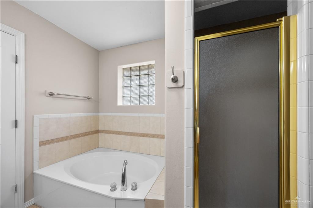 6020 North Doolittle Road Edinburg, TX 78542 - Photo 12 of 23 Corner soaking tub featuring deck-mounted chrome fixtures, surrounded by tiled walls with an accent band, and a glass block window