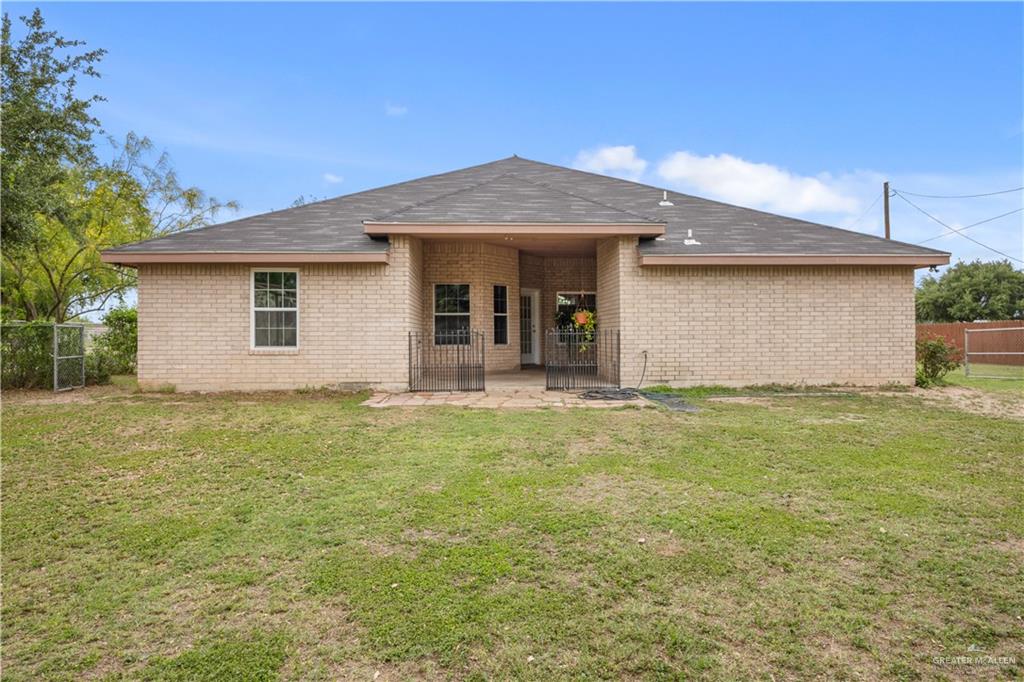 6020 North Doolittle Road Edinburg, TX 78542 - Photo 15 of 23 Rear exterior featuring light brick masonry, a dark shingle roof, a covered patio area, and a large grassy yard
