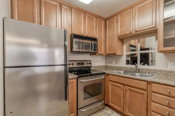 a kitchen with stainless steel appliances granite countertop a refrigerator a stove a sink and dishwasher with wooden floor