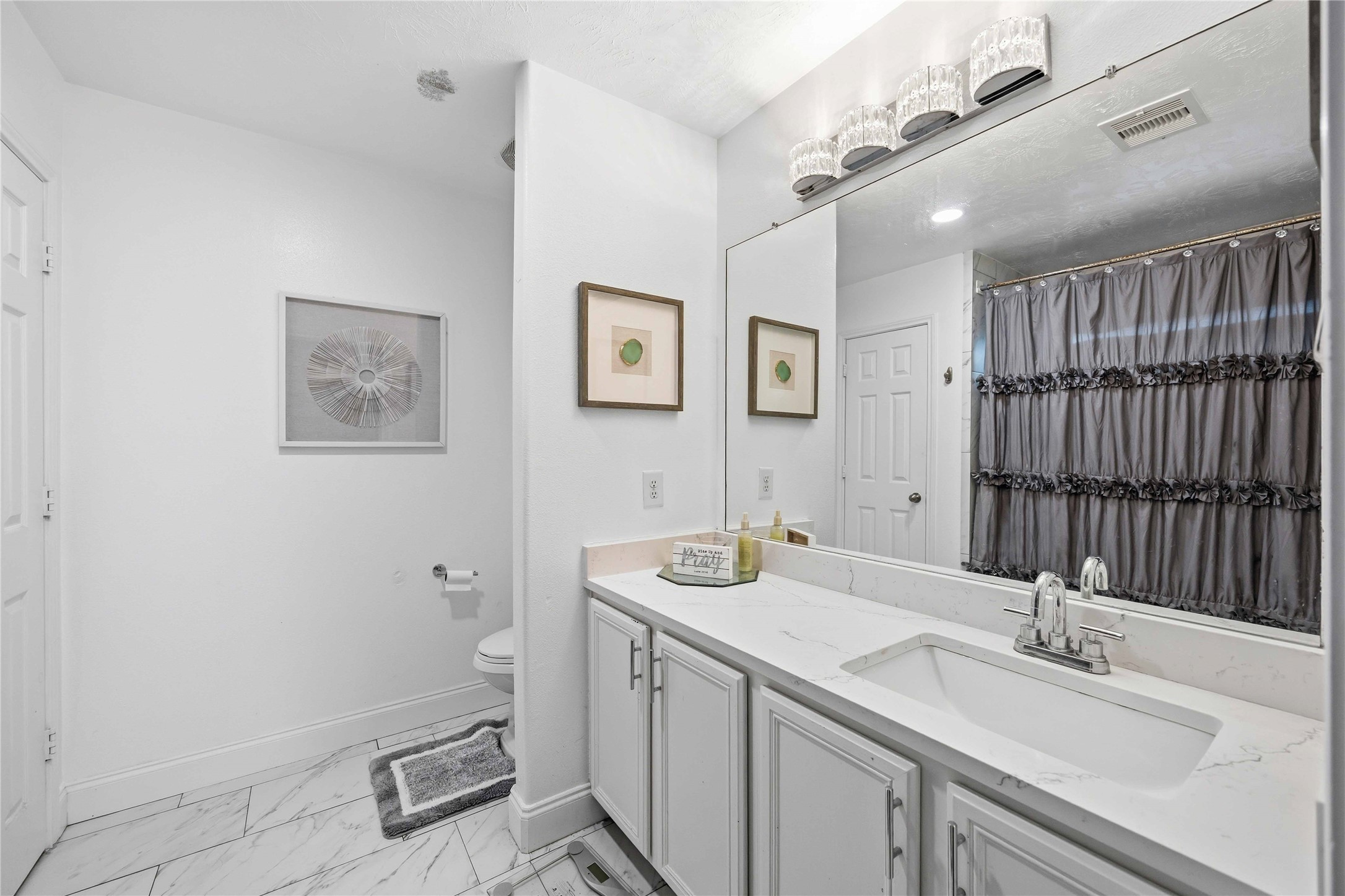 3538 Maris Way Humble, TX 77338 - Photo 13 of 24 Bright and well-appointed bathroom featuring a dual-sink vanity, expansive framed mirror, and sleek modern lighting. Clean white finishes and marble-look tile flooring create a fresh, polished look with functional storage.