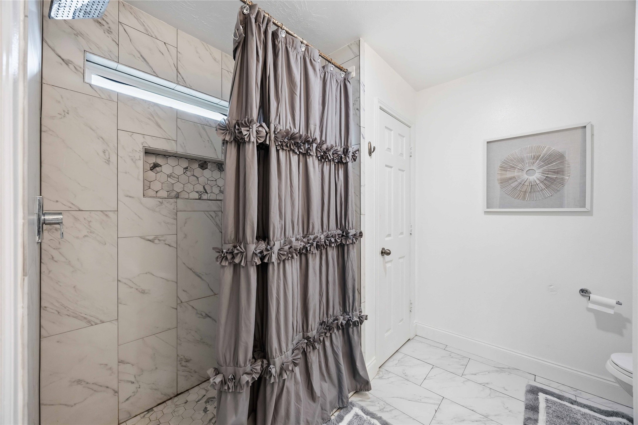 3538 Maris Way Humble, TX 77338 - Photo 14 of 24 Modern walk-in shower featuring full tile surround, decorative inset niche, and sleek contemporary finishes. Marble-look tile flooring and clean lines create a bright, spa-inspired feel.