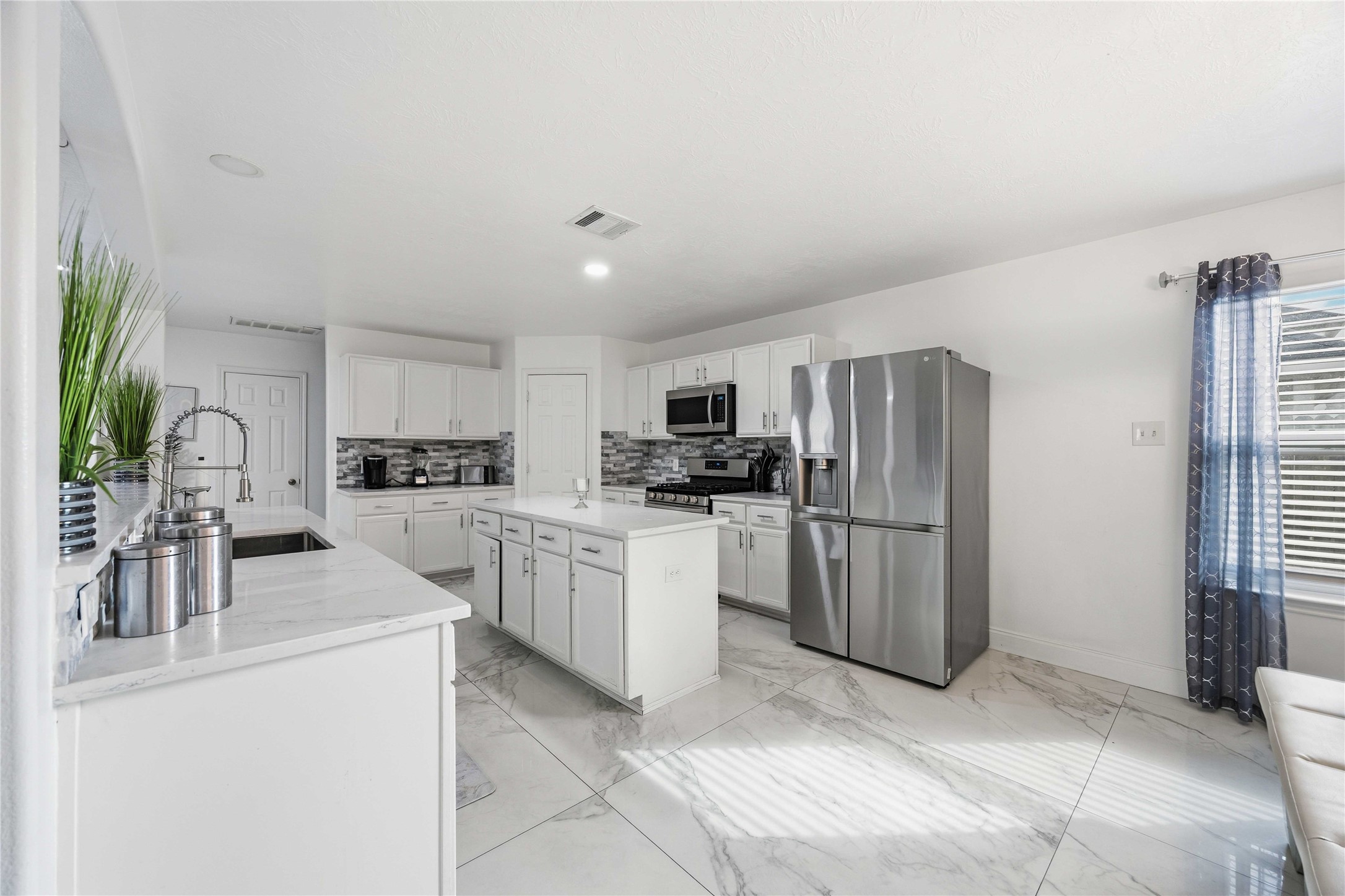 3538 Maris Way Humble, TX 77338 - Photo 22 of 24 Bright, open kitchen featuring white cabinetry, granite-style countertops, stainless steel appliances, and a spacious center island. Marble-look tile flooring and abundant natural light create a clean, modern setting ideal for everyday living and entertaining.