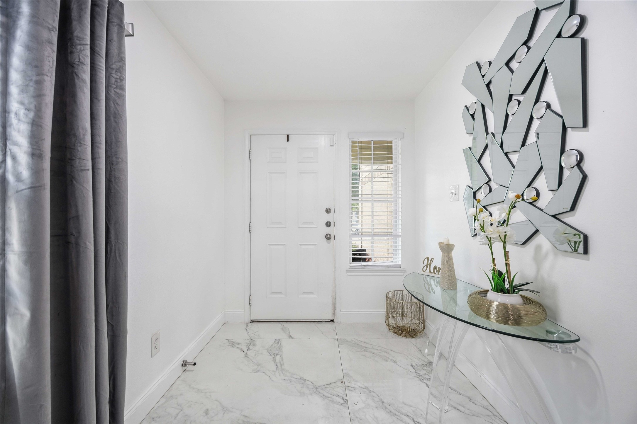 3538 Maris Way Humble, TX 77338 - Photo 4 of 24 Bright and elegant entry foyer featuring sleek marble-look tile flooring, fresh neutral walls, and abundant natural light. The space is accented by a modern glass console table and decorative mirror, with a nearby window adding warmth and openness. A clean, welcoming transition into the main living areas of the home.