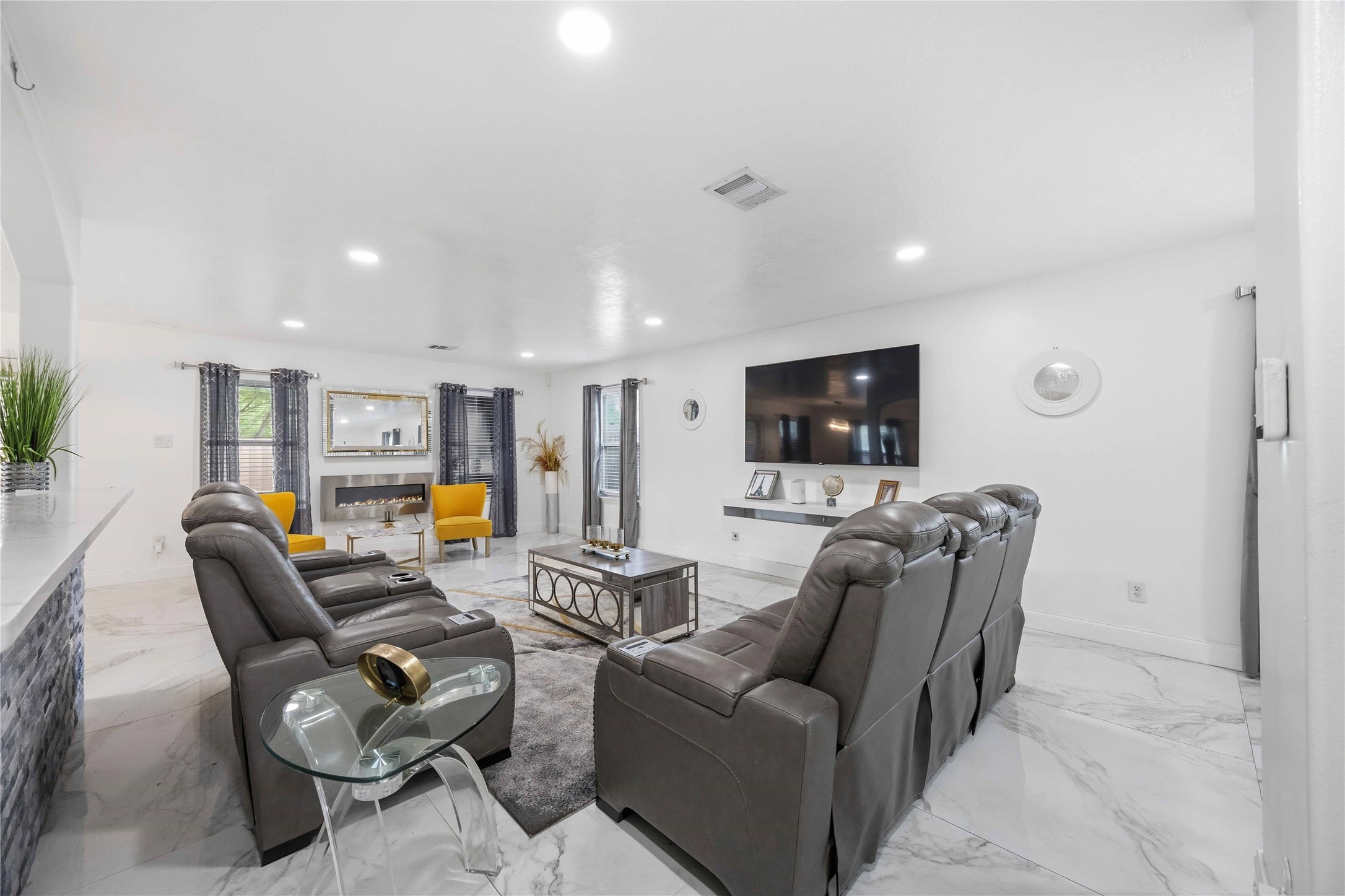 3538 Maris Way Humble, TX 77338 - Photo 6 of 24 Contemporary living room showcasing sleek marble-look tile flooring, recessed lighting, and an open, airy layout. The space features comfortable seating arranged around a mounted media center, creating a stylish yet functional gathering area. Neutral tones are accented by modern décor and natural light, offering a seamless flow to adjacent living and dining spaces—perfect for entertaining or relaxing.