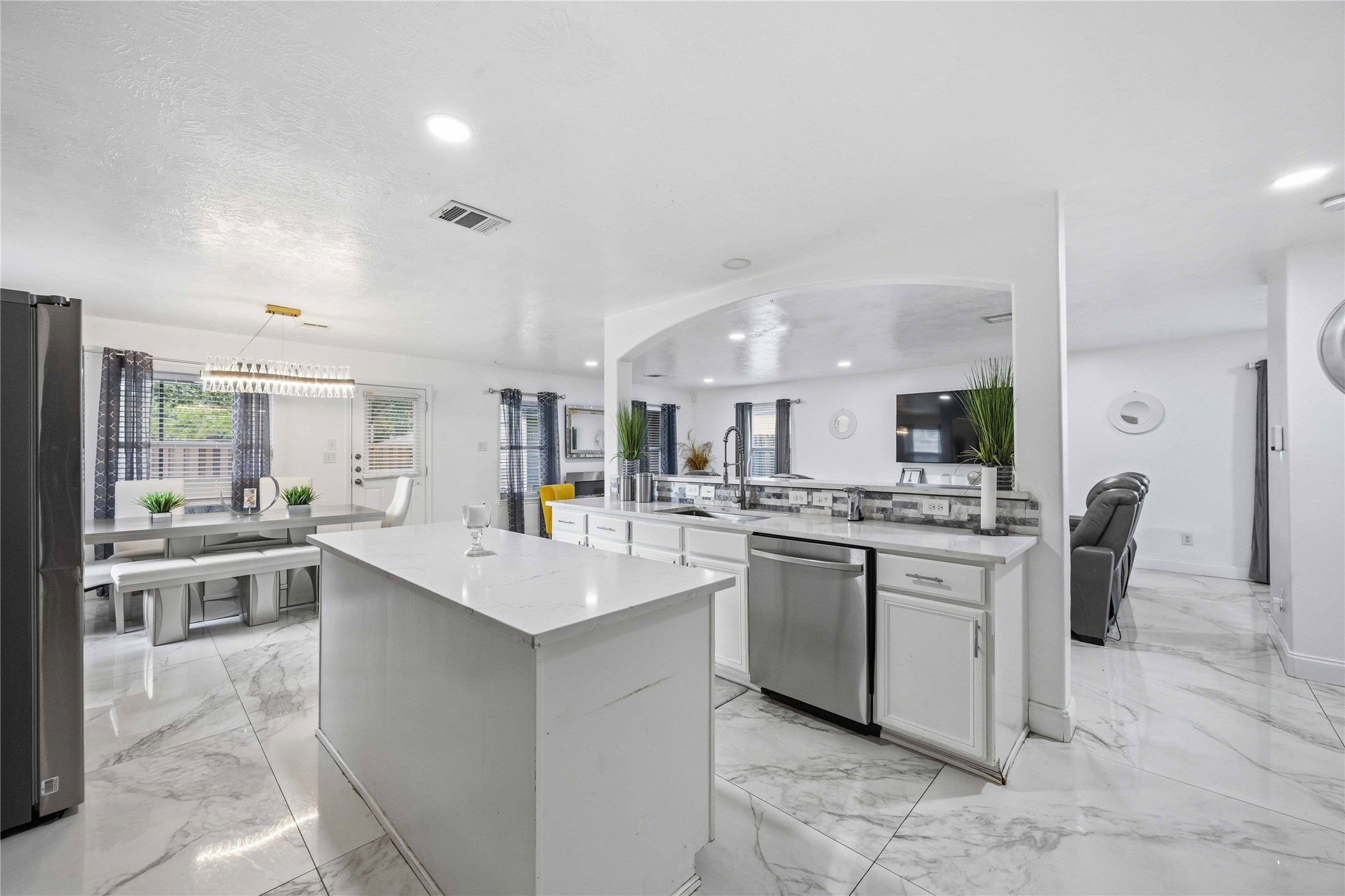 3538 Maris Way Humble, TX 77338 - Photo 9 of 24 Spacious open-concept kitchen featuring a large center island, granite-style countertops, and crisp white cabinetry throughout. Marble-look tile flooring, stainless steel dishwasher, and modern fixtures enhance the contemporary design. The kitchen flows seamlessly into the dining and living areas under vaulted ceilings and recessed lighting, creating an ideal layout for entertaining and everyday living.