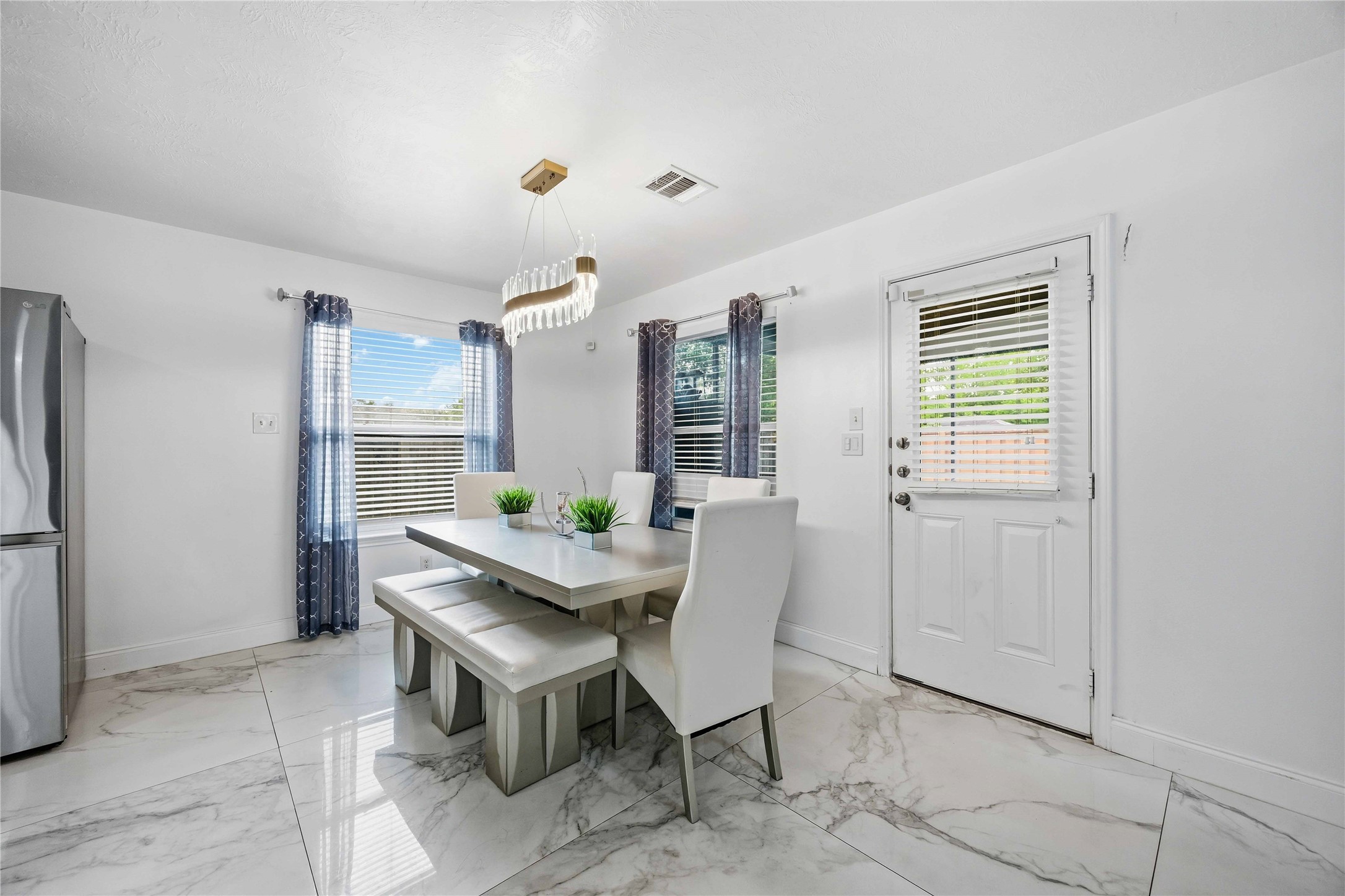 3538 Maris Way Humble, TX 77338 - Photo 10 of 24 Bright and inviting dining area featuring elegant marble-look tile flooring, a modern chandelier, and ample natural light from multiple windows. The space comfortably accommodates a full dining set and offers a seamless connection to the kitchen, making it ideal for gatherings and everyday meals. A nearby exterior door provides convenient backyard access and enhances the open, airy feel of the space.