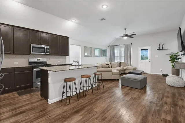 a open kitchen with stainless steel appliances granite countertop a stove top oven a sink dishwasher a dining table and chairs with wooden floor