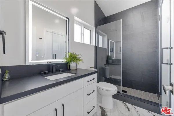 a bathroom with a granite countertop sink a toilet a mirror and shower