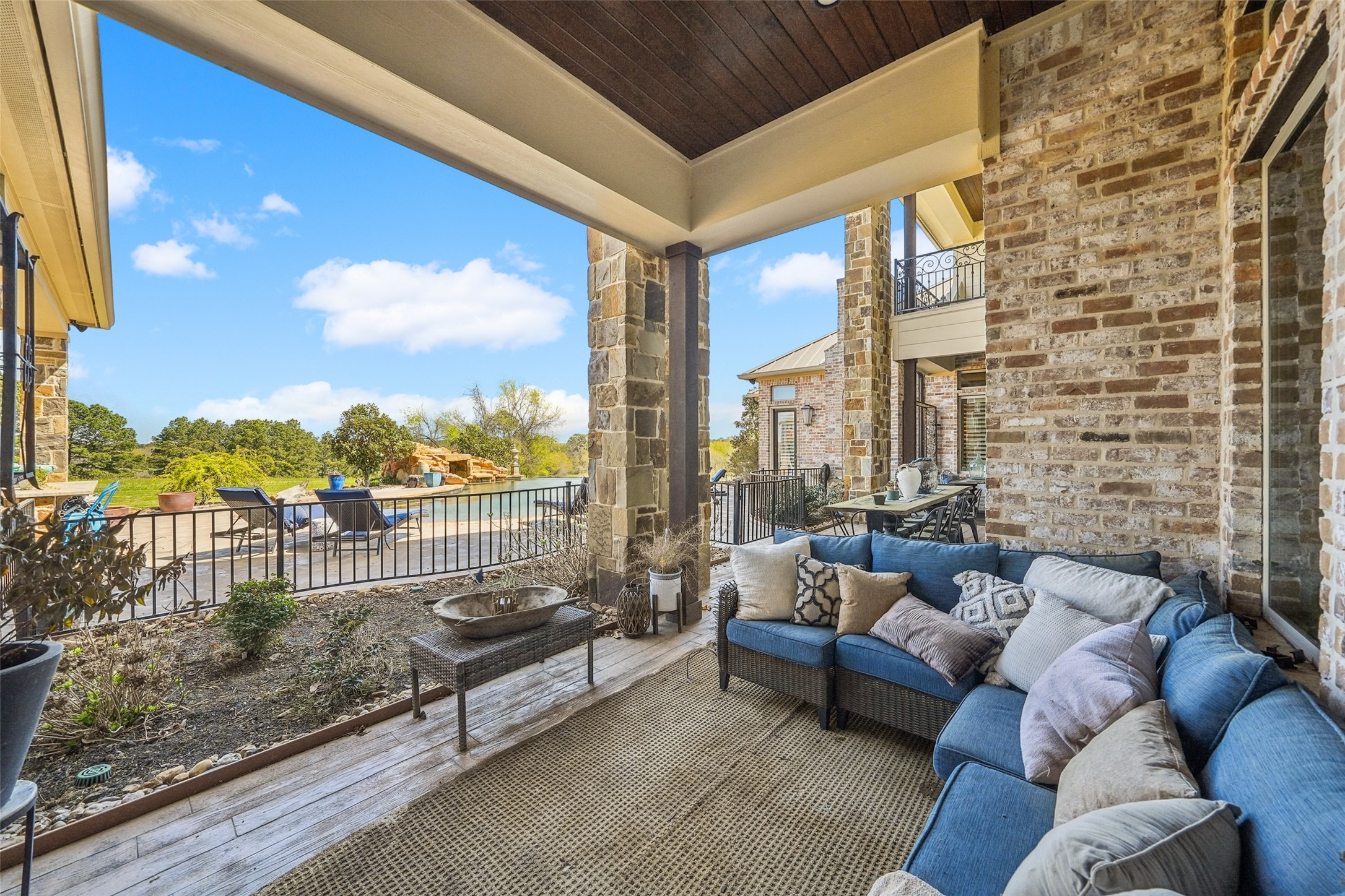 460 Bishop Road Huntsville, TX 77320 - Photo 33 of 50 The spacious outdoor patio and balcony area with a rustic-modern design. The space features brick walls, stone columns, and a covered ceiling. The patio extends to an open area overlooking a pool, landscaped garden, and surrounding greenery.