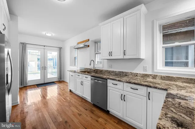 a kitchen with granite countertop a stove a sink and white cabinets with wooden floor