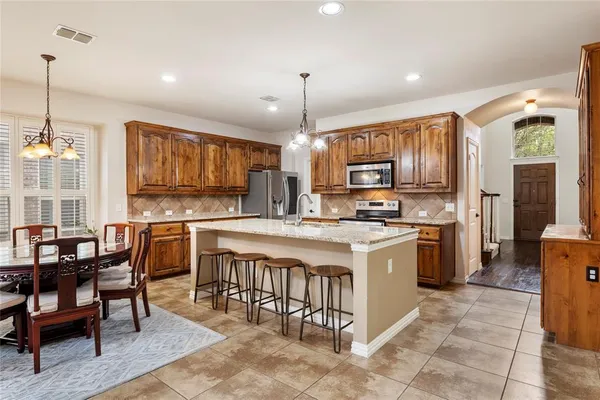 a kitchen with stainless steel appliances granite countertop a stove top oven a refrigerator a sink dishwasher a dining table and chairs with wooden floor