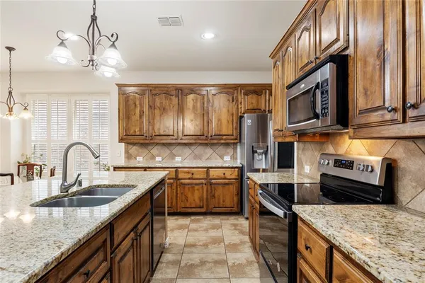 a kitchen with stainless steel appliances granite countertop a sink a stove and a wooden cabinets
