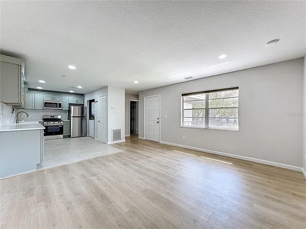 an empty room with wooden floor kitchen view and a window