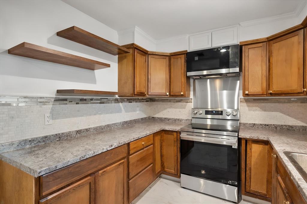 3400 Emhouse Road Corsicana, TX 75110 - Photo 25 of 34 Kitchen featuring warm wood cabinetry, granite-style countertops, mosaic tile backsplash, stainless steel appliances, and floating wood shelves