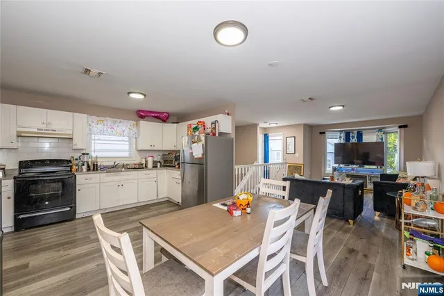 a kitchen with stainless steel appliances kitchen island granite countertop a refrigerator a stove top oven a sink dishwasher and white cabinets with wooden floor