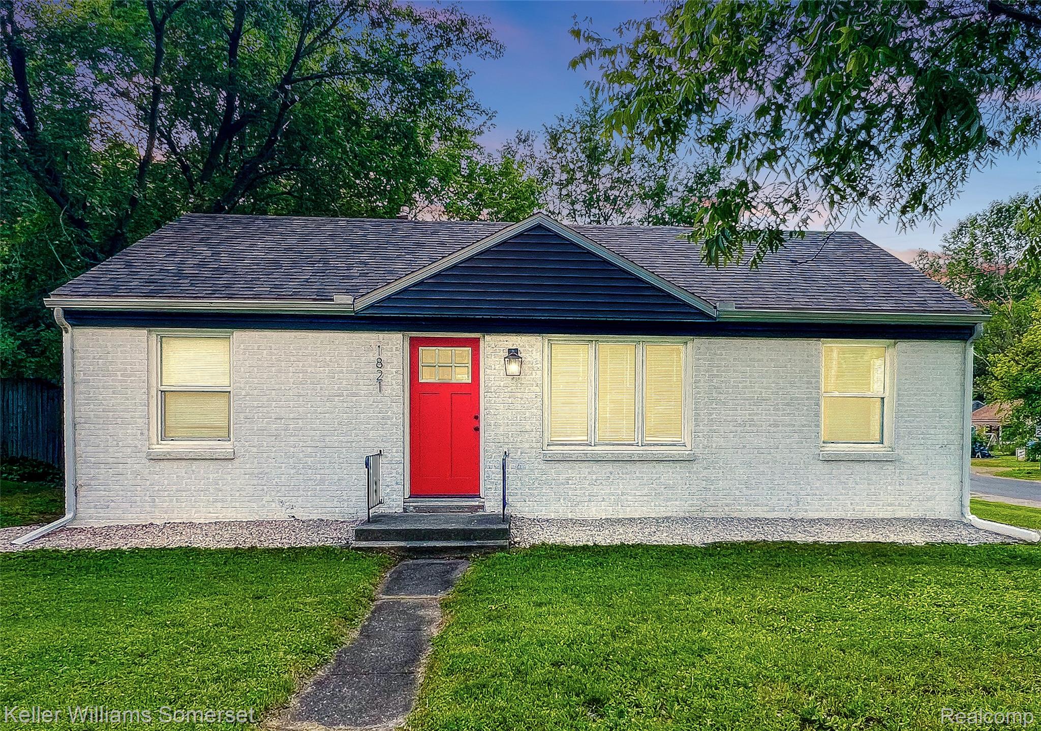 1821 Nazareth Road Kalamazoo, MI 49048 - Photo 1 of 20 Single-story residence featuring white painted brick, a bold red entry door, dark gray architectural shingle roofing, and a contrasting dark blue accent gable