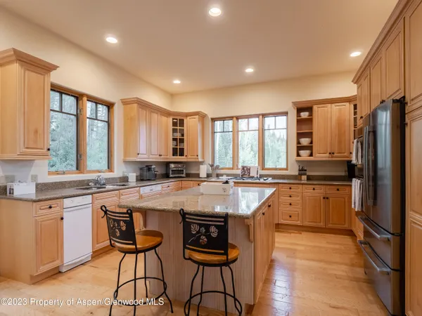 a large kitchen with kitchen island granite countertop a stove a sink a refrigerator and white cabinets with wooden floor