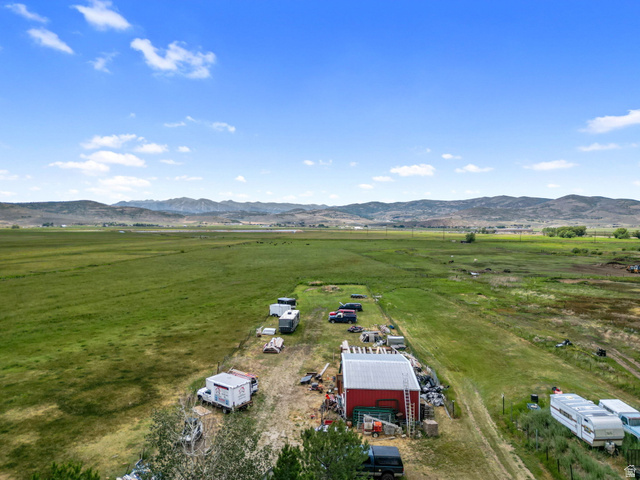 490 South Main Street Kamas, UT 84036 - Photo 24 of 25 Expansive rural property featuring a red barn with a metal roof, surrounded by green pastureland, a gravel drive, and distant mountains under a blue sky