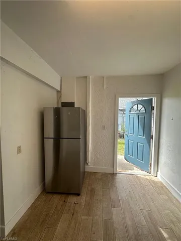 a view of a refrigerator in kitchen and an empty room with wooden floor
