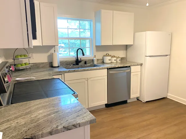 a kitchen with stainless steel appliances granite countertop a refrigerator a sink dishwasher a stove with white cabinets and wooden floor