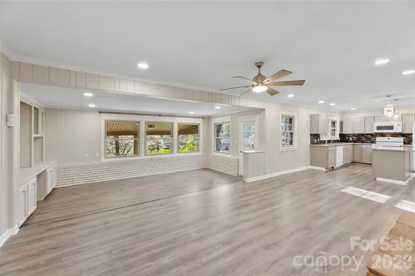 a view of an empty room with wooden floor and a kitchen