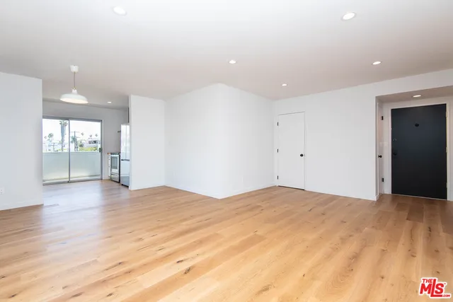 a view of an empty room with wooden floor and a kitchen