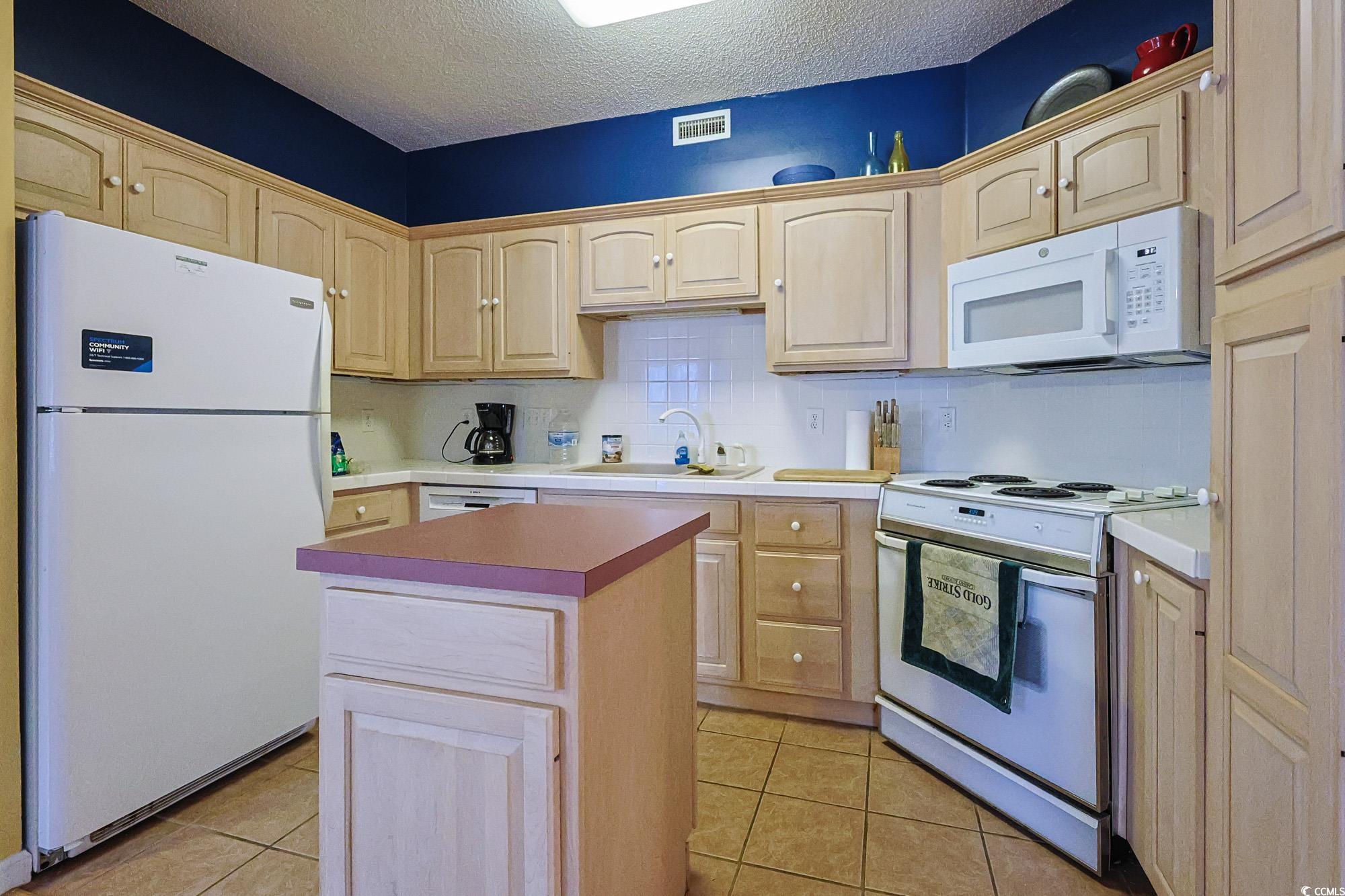 2302 Sweetwater Boulevard, Unit 2302 Murrells Inlet, SC 29576 - Photo 10 of 24 Kitchen featuring white appliances, tasteful backsplash, light brown cabinetry, and a textured ceiling